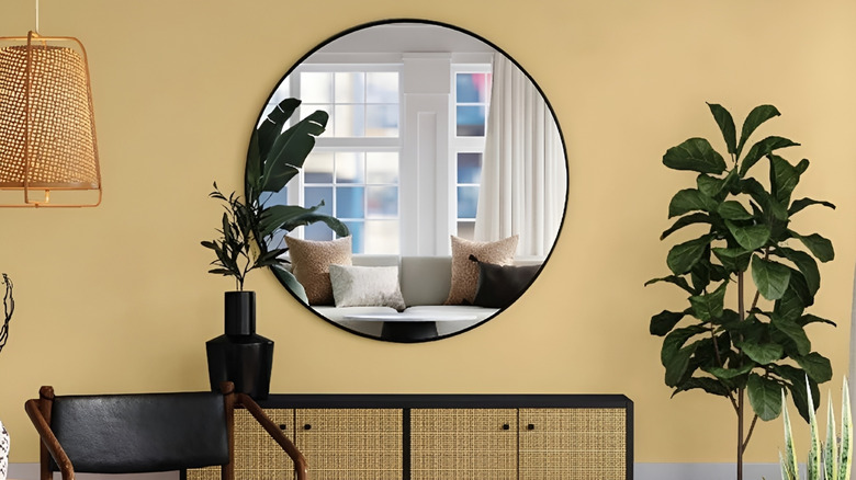 Large round mirror in house reflecting window and sofa across from it.
