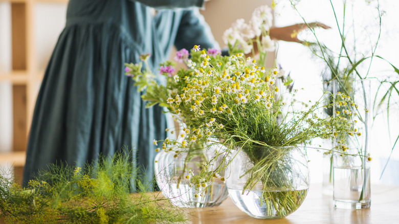 A woman arranges bouquets of wildflowers in clear glass vases.