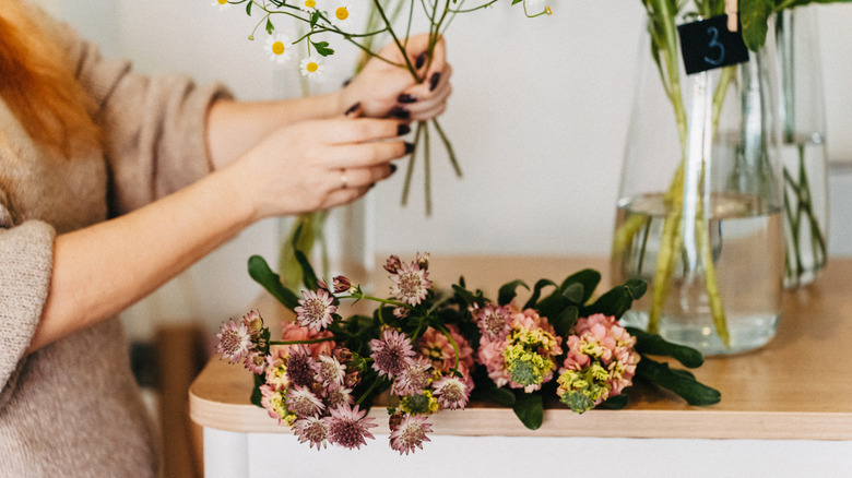 Woman arranges a wildflower bouquet with flowers lying on the table ready to be used.