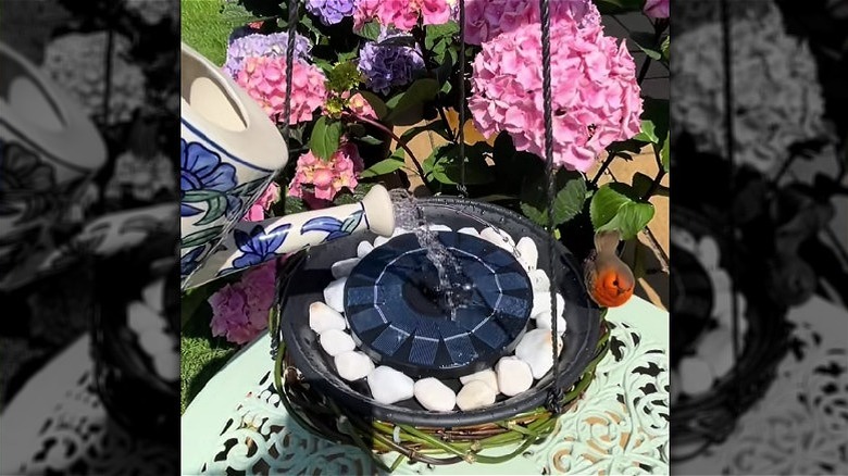 Watering can filling a hanging solar bird bath in garden.