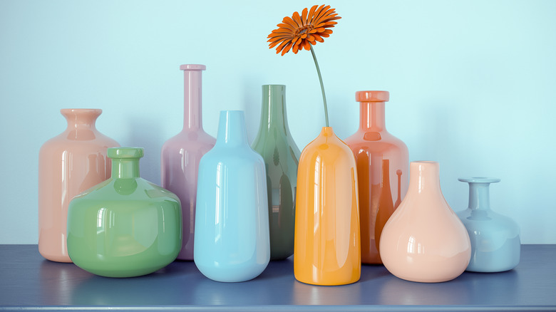 empty pastel vases with one flower rest on a blue countertop against light blue wallpaper