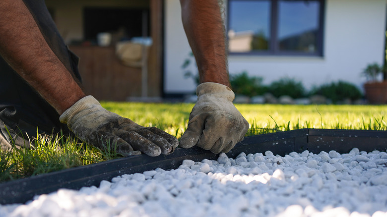 A gardener installs a decorative garden edge made of white landscaping rocks.