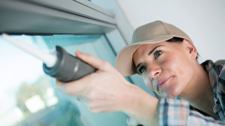 Woman caulking a window pane. 