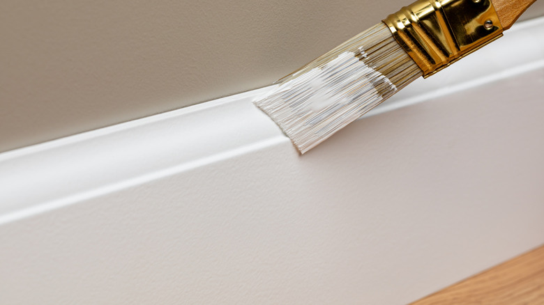 Trim brush painting baseboards with white paint