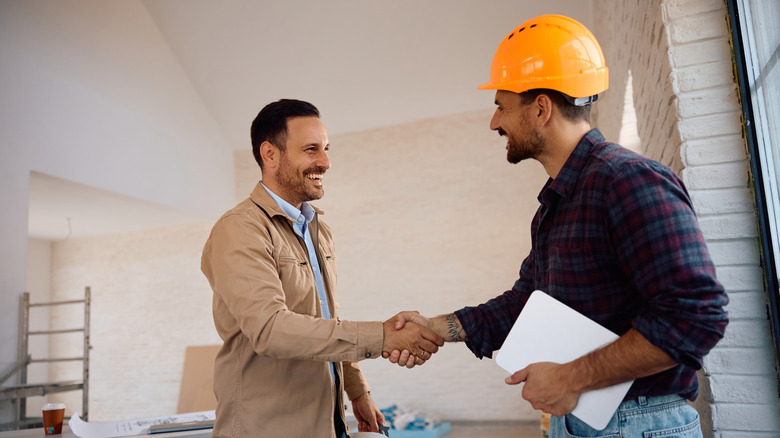 A man shaking hands with a male home contractor in an orange safety helmet
