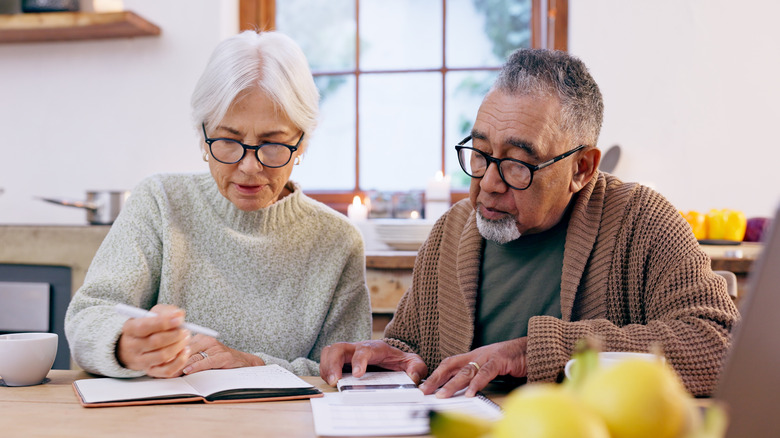 A senior man and woman are budgeting at their kitchen table
