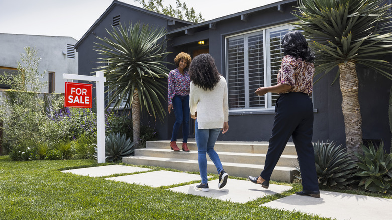 People walking up to a house with a "for sale" sign outside