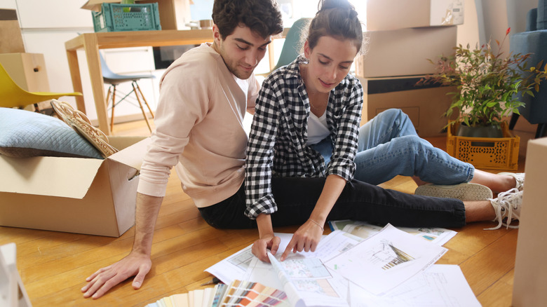 A couple looks at papers on the floor, discussing home renovation