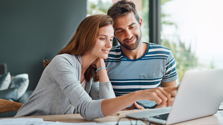 A man and woman point at a laptop, researching together