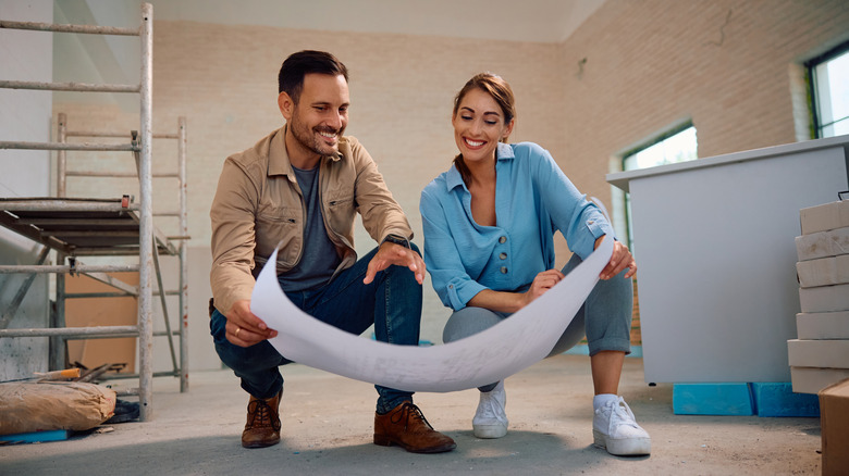 A man and a woman smile as they look at renovation plans together