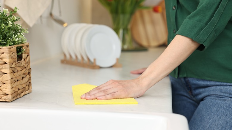person wiping white countertop with yellow cloth