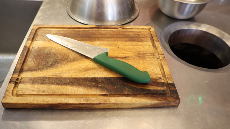 A stainless steel countertop with scratches and a wooden cutting board