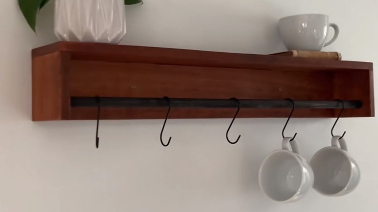 A small wood shelf with a curtain rod and S-hooks with mugs hanging from them.