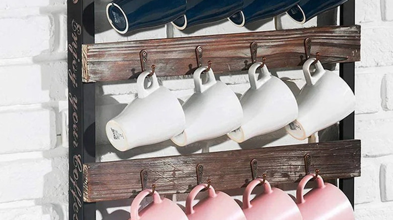 A decorative wooden wall ladder coffee mug rack fitted with hooks that blue, white, and pink mugs hang from.