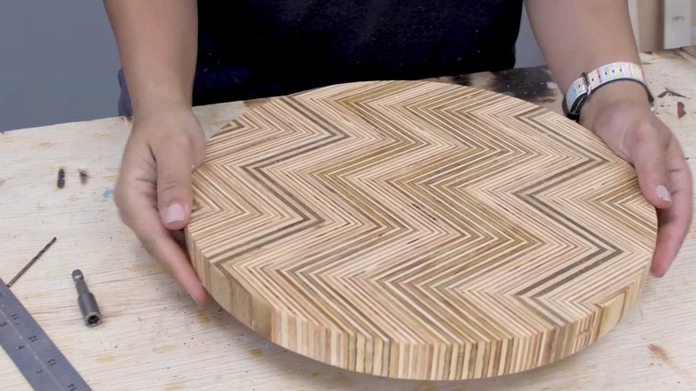 A person holds a patterned lazy Susan made out of plywood between her hands.