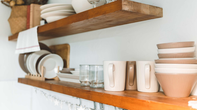 Coffee mugs and other crockery on a pair of floating shelves mounted to the wall in a kitchen.