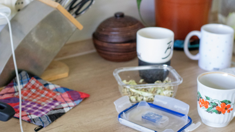 Coffee mugs and other kitchen items on a cluttered countertop.