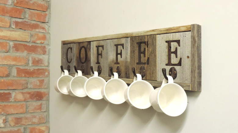 Mugs hang from hooks on a piece of barn wood wall art adorned with lettering.