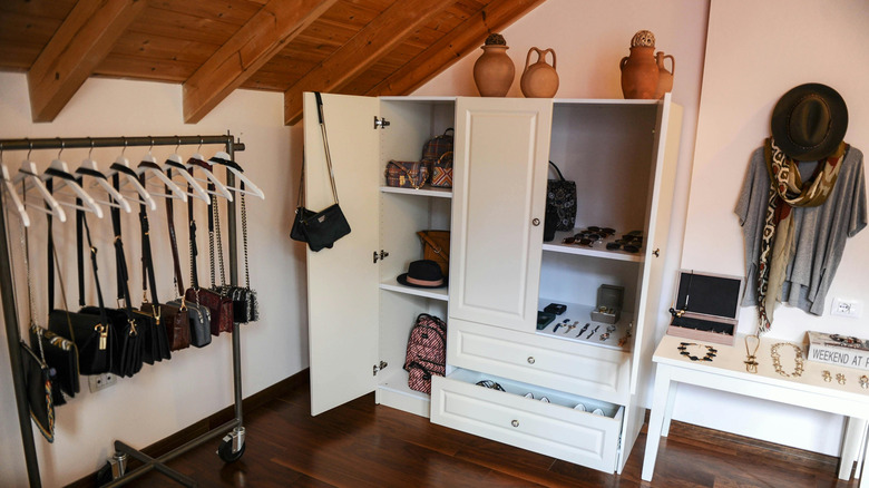 A small attic closet with an exposed wood ceiling and hardwood floors is full of accessories