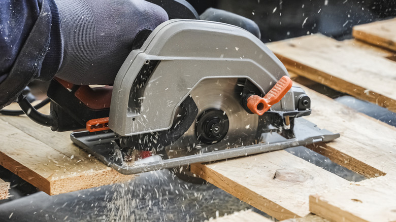 A man using a circular saw to cut up a pallet for a recycled woodworking project