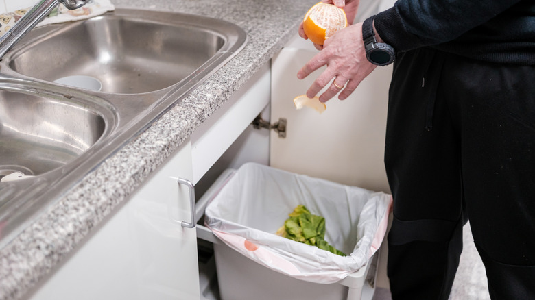 Man throwing orange peel in a compost bin under the kitchen sink.