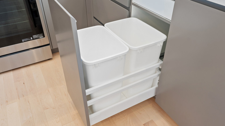 A kitchen with a silver oven and a white trash can. The trash can is in a drawer with two other trash cans.