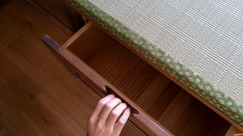 A hand reaching out and opening a dark wooden drawer.