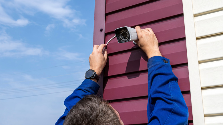 Man installing an outdoor camera on side of house