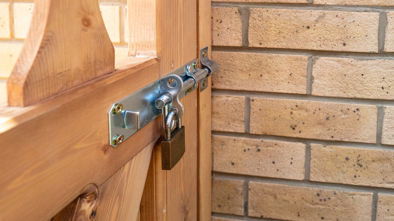 Close-up of sliding bolt mechanism with padlock on wooden fence
