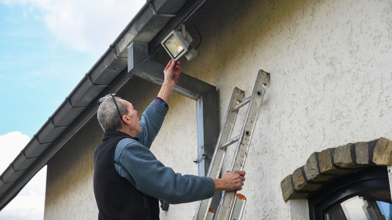 Man installing LED light on side of house