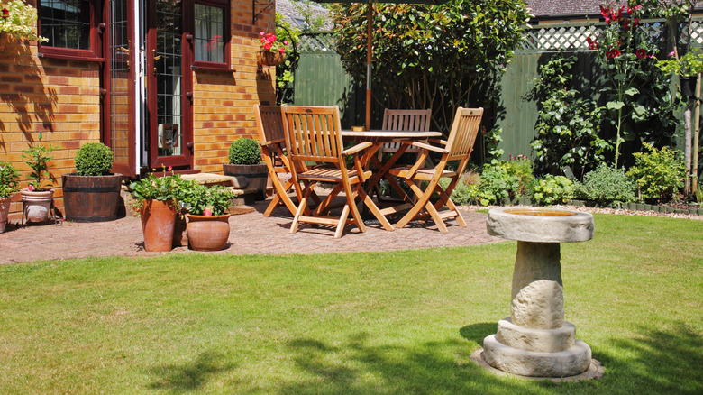 A backyard lawn is filled with patio furniture and a birdbath.