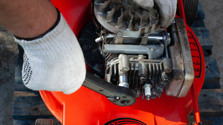 Close-up of a man unscrewing a lawn mower oil filter with a torque wrench