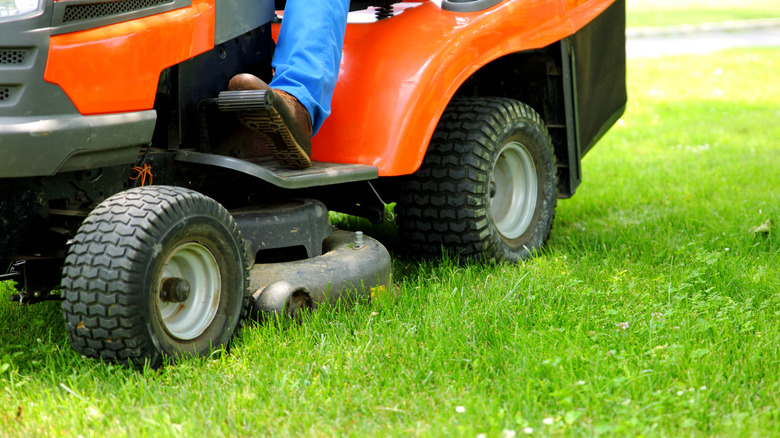 Close-up of a person trimming grass with a riding lawn mower