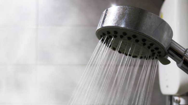 A close up of a shower head with hot water coming out and steam in the background