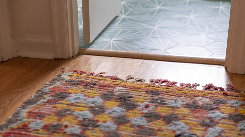 A colorful rug on a wood floor and patterned tile