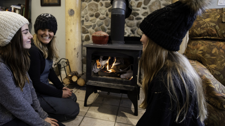 A group of young women gather around a woodstove.