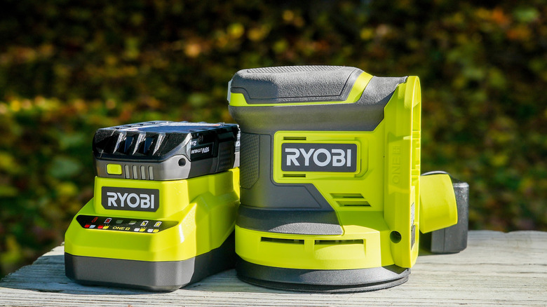 Close-up of Ryobi ONE+ cordless power sander and lithium-ion battery with charger, showcasing the bright green and black design, ideal for DIY and woodworking projects outdoors.