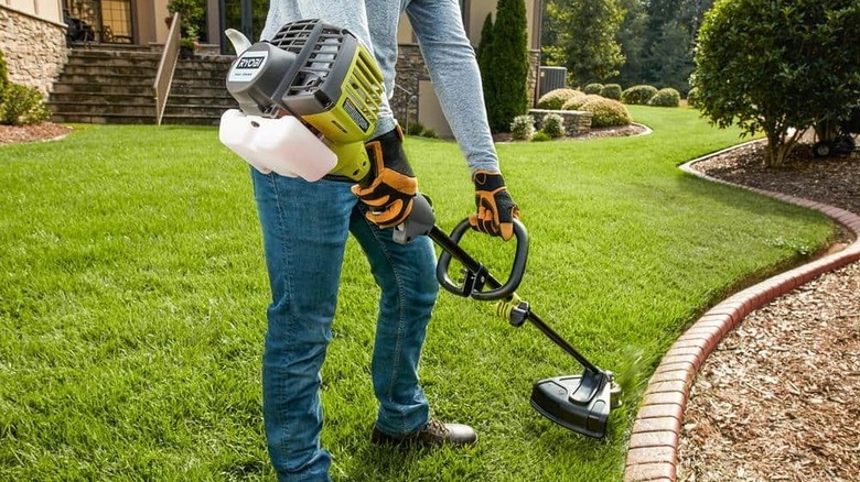 someone using a gas-powered Ryobi string trimmer on a lawn
