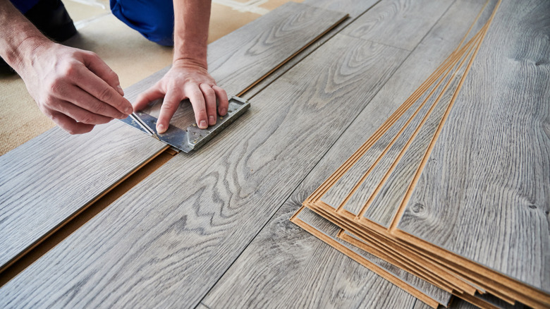 A male worker using metal construction ruler and pen while drawing line on laminate flooring board.