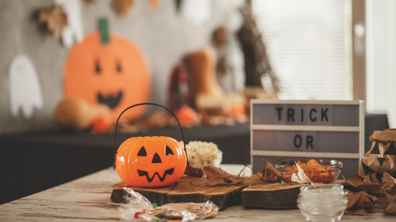 Halloween table with sign that says TRICK OR TREAT, plastic pumpkin, and wood boards while a pumpkin cutout is in the background