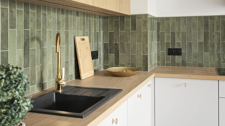 Kitchen space with bamboo counters, green backsplash, black sink, and brass fixtures
