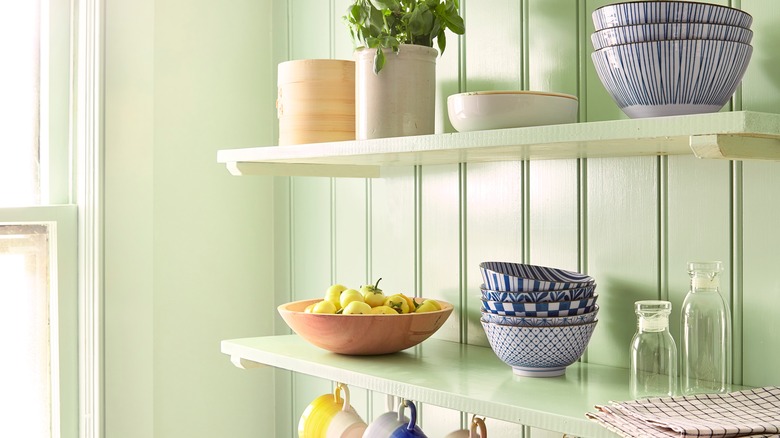 An open shelf kitchen with two shelves holding dishes and decor in a bright color scheme