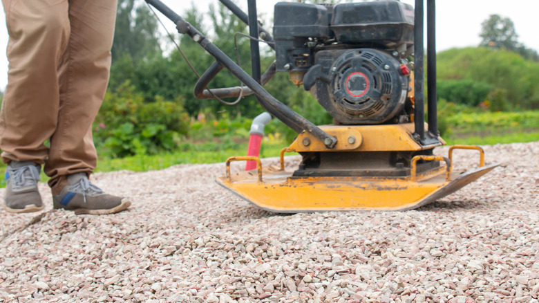 A man using a vibrating plate to compact rubble as the base for a gravel drive