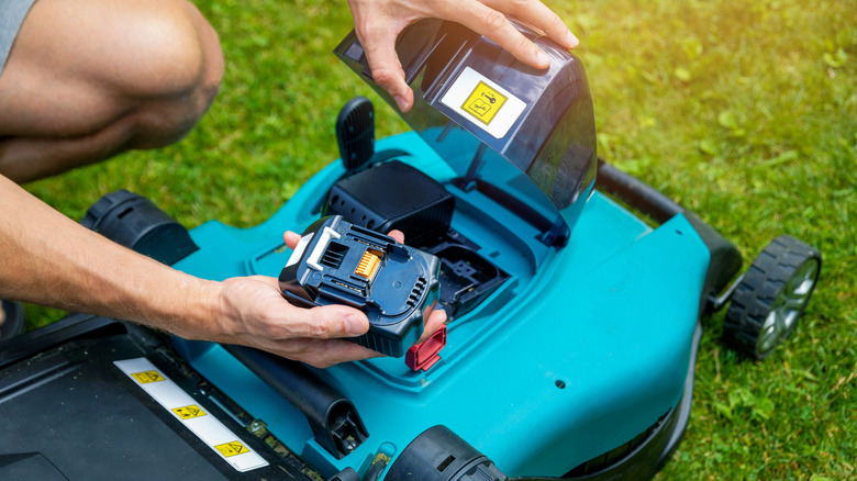 A man putting battery into electric cordless lawn mower.