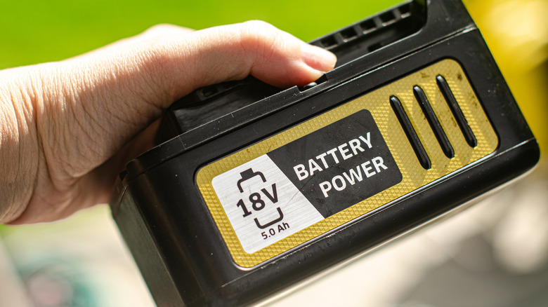 A hand holding a battery for a cordless lawn mower.