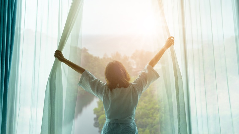 Woman opening bedroom curtains