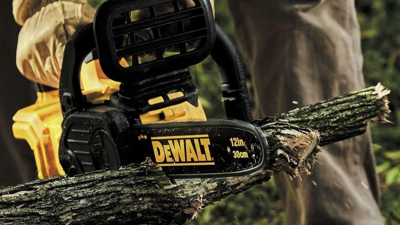 Person cutting a small branch with a 12-inch DeWalt chainsaw
