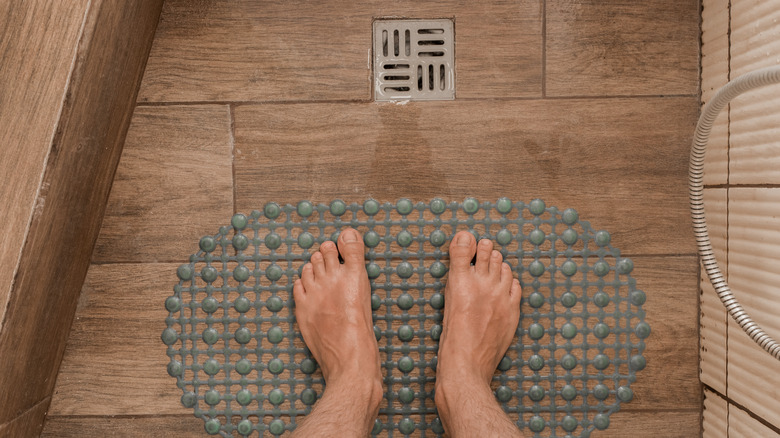 Man standing on a mat with water draining to point drain in a shower