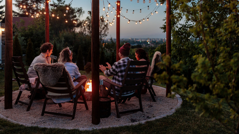 A group of people sit around a circular gravel fire pit