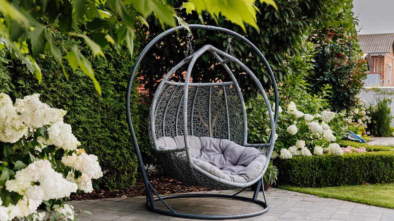An egg-shaped freestanding patio swing amidst lush greenery.